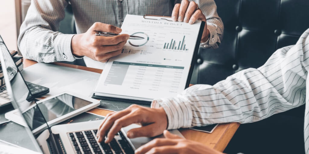 Two business professionals reviewing financial reports and cash flow charts on a clipboard and laptop during a planning meeting focused on recession-proofing strategies.